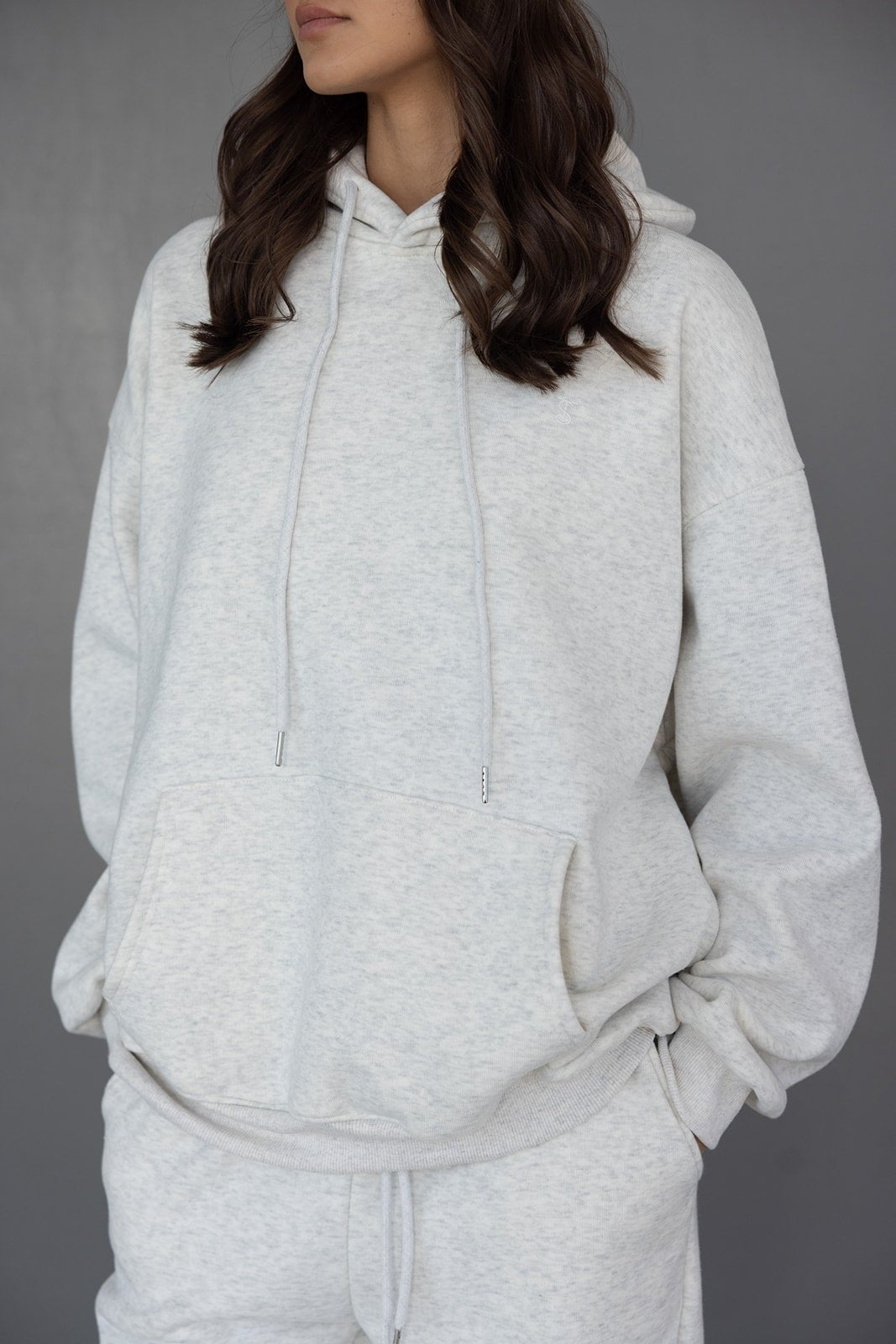 אישה לובשת סט טרנינג אפור בהיר עם קפוצ'ון וכיס קדמי, אופנת נשים נוחה ליום יום