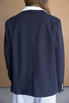 אישה לובשת בלייזר כחול עם צווארון לבן וכפתורים זהובים, צילום מגב, בגדי נשים אופנתיים