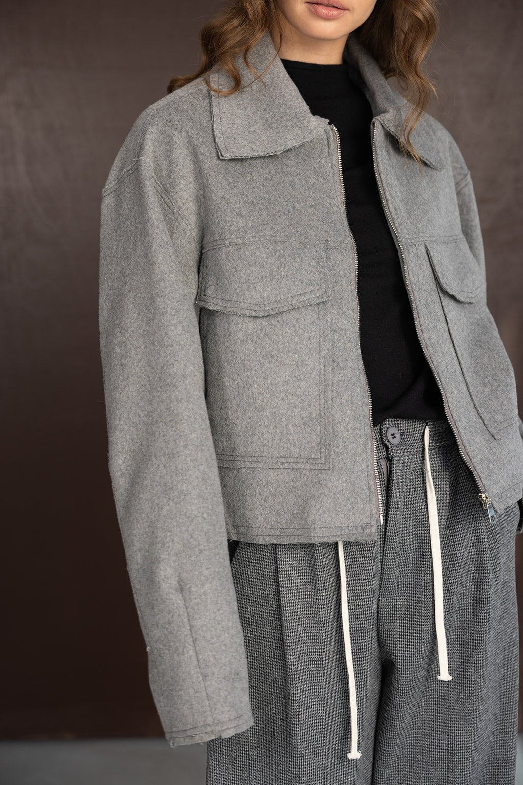 אישה לובשת מעיל קצר אפור ובוקסר מכנס מחויט בגווני אפור אופנתי, רקע חום.