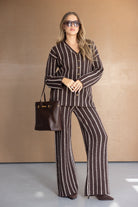 אישה לובשת חליפת נשים חומה מפוספסת, מחזיקה תיק חום ונועלת נעלי עקב, אופנת חורף