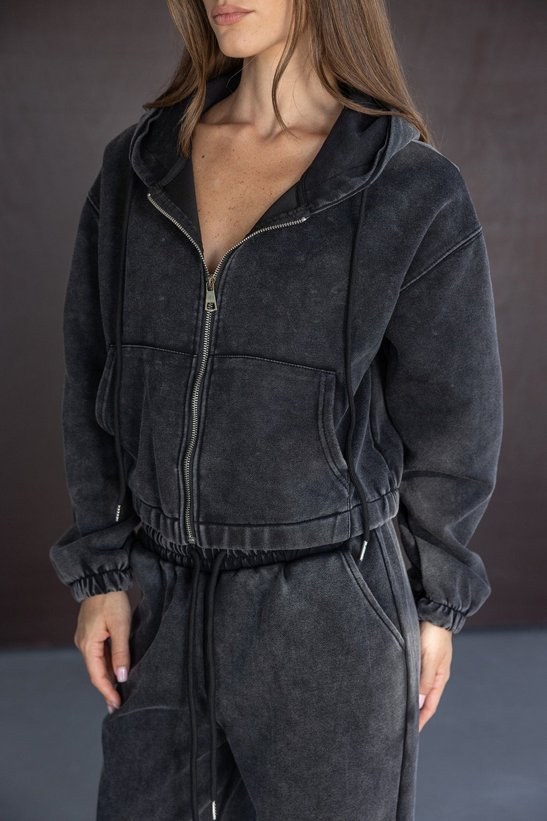 אישה לובשת סט טרנינג נשים אופנתי, צבע שחור דהוי, רוכסן קדמי וכובע קפוצ'ון