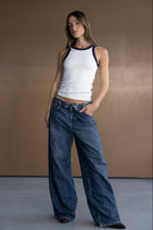 דוגמנית לובשת גופיית נשים לבנה עם שוליים כהים ומכנסי ג'ינס רחבים, אופנת רחוב עדכנית