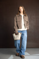 אישה עם ז'קט חום, ג'ינס רחב, סוודר לבן, תיק בד ונעליים חומות – אופנת חורף לנשים