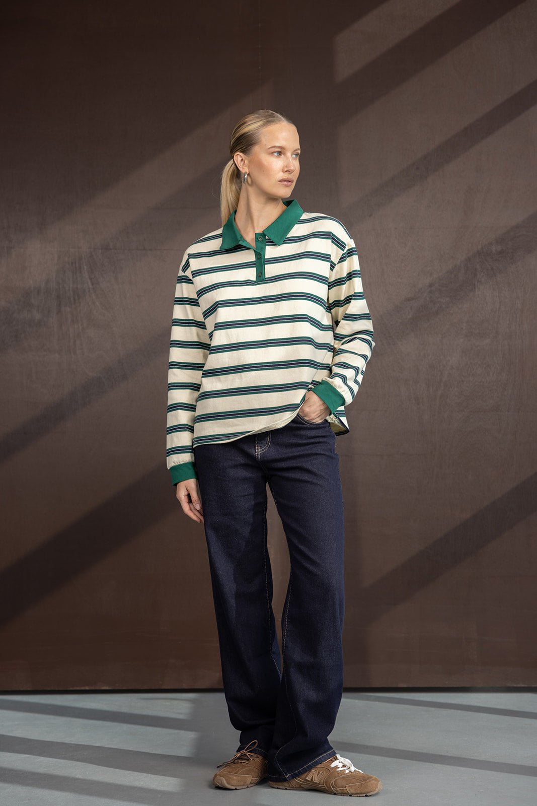 אישה לובשת חולצת פסים ירוקה ולבנה עם צווארון ירוק, ג'ינס כהה ונעלי סניקרס חומות, אופנת נשים קז'ואל