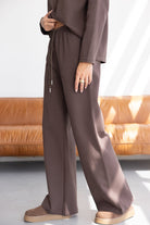 סט טרנינג חום לנשים, בד רך ונעים, מכנס רחב וסווטשירט, נעלי בית חומות, רקע סלון מודרני