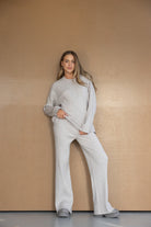 אישה לובשת סט סוודר ומכנסיים סרוג בצבע אפור בהיר אופנתי, רקע נייטרלי