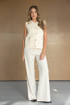 דוגמנית לובשת גופיית סריג שמנת עם כפתורים וכיסים ומכנסי בד רחבים בצבע שמנת, אופנת נשים עדכנית