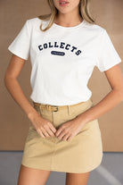 דוגמנית לובשת חולצת טי לבנה עם הדפס 'COLLECTS FREEDOM' וחצאית מיני בז׳ אופנתית לנשים