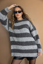 דוגמנית לובשת סוודר פסים אפור כהה ואפור בהיר, משקפי שמש שחורים, חצאית שחורה וגרביון, אופנה לנשים