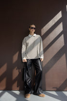 אישה עם חולצת פסים ארוכה ומכנסי דמוי עור שחורים, משקפי שמש ואביזרי אופנה, מראה אופנתי צעיר