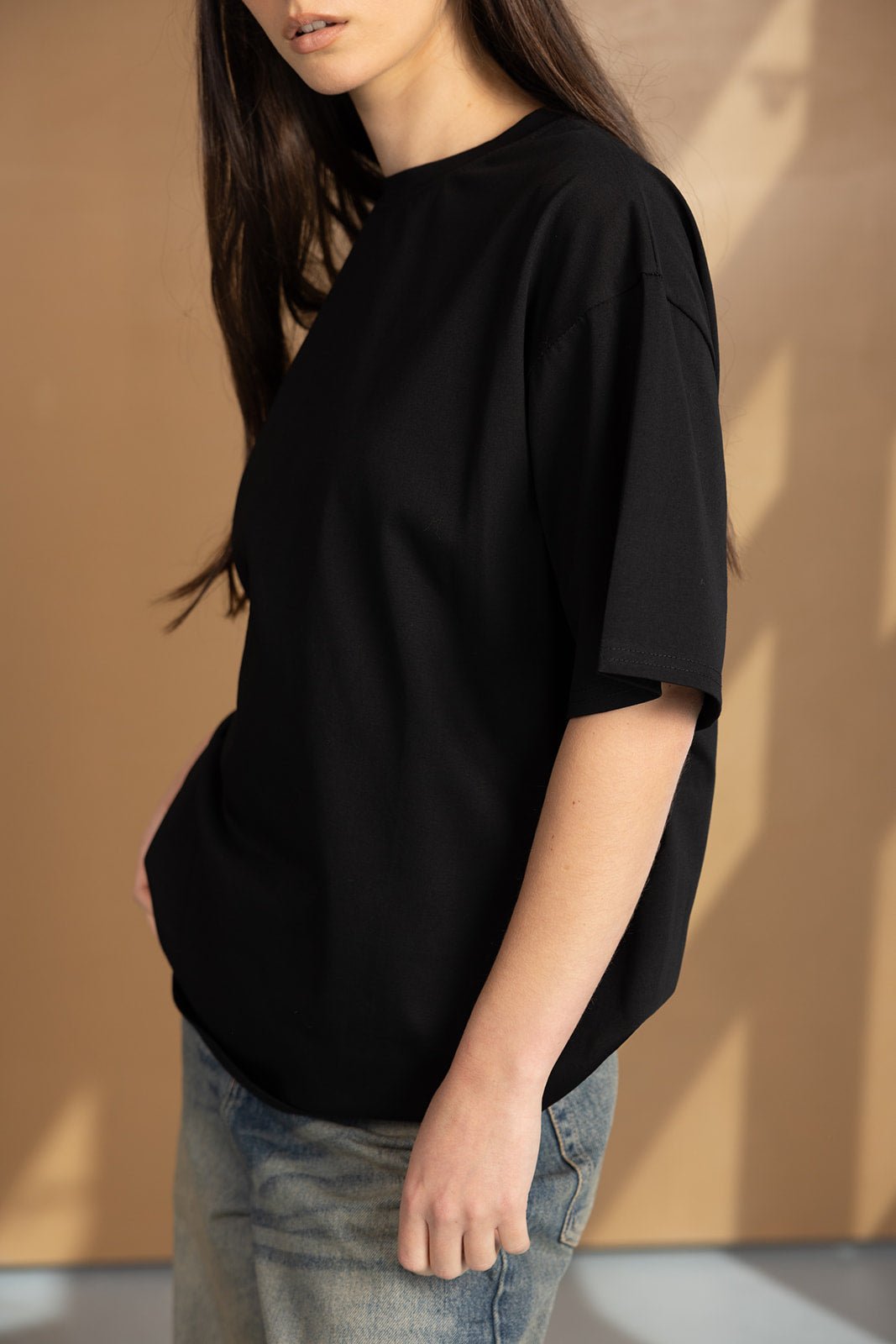 אישה עם שיער ארוך לובשת טי שירט שחורה וג'ינס אופנתי, אופנת נשים צעירה