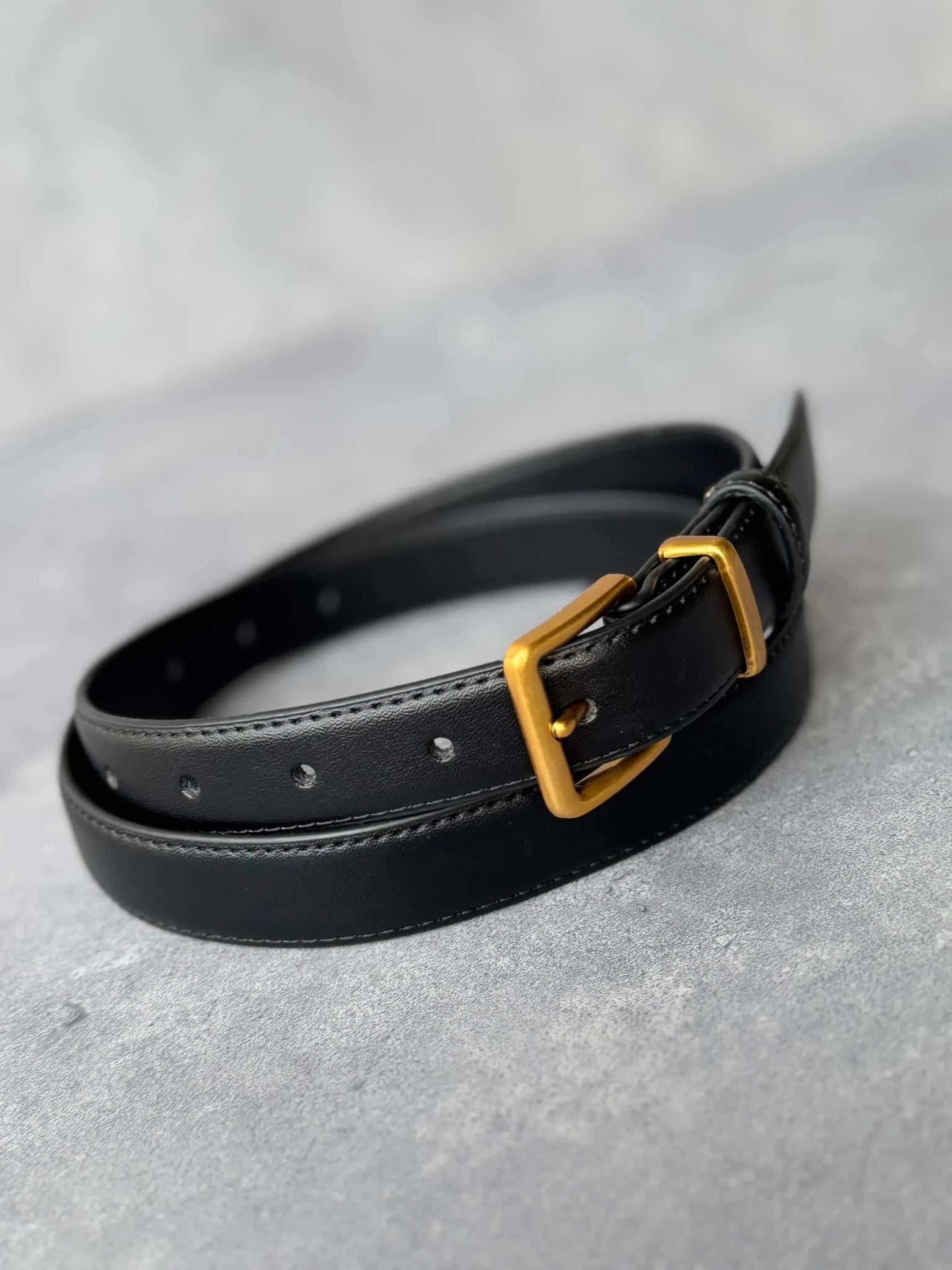 חגורת עור שחורה עם אבזם זהב, אופנת נשים ונערות, מצולמת על רקע אפור