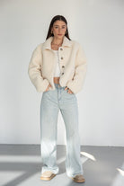 דוגמנית לובשת ג'קט בוקסה קרם עם כפתורים, ג'ינס בגזרה רחבה ונעליים בהירות, אופנת נשים עדכנית