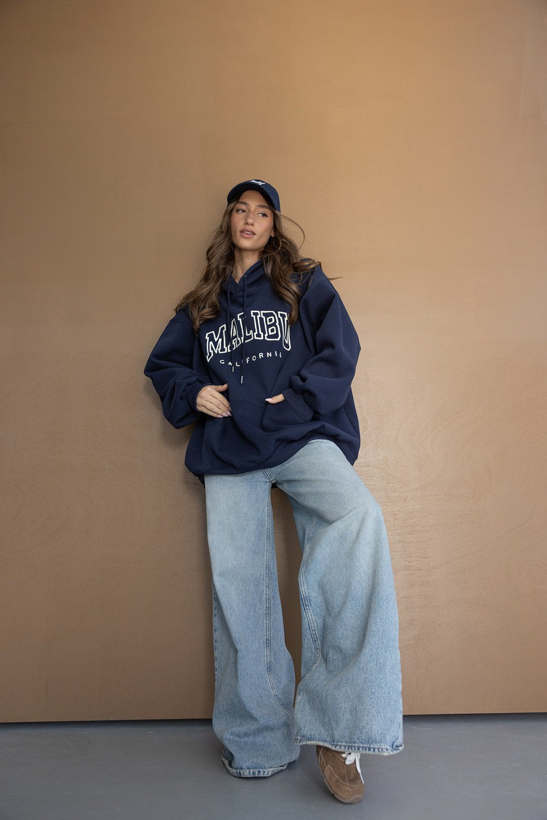 אישה צעירה עם קפוצ'ון כחול MALIBU, ג'ינס רחב וכובע כחול, לוק קז'ואלי אופנתי לנערות
