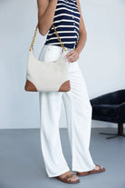 אישה לובשת חולצת פסים כחולה ולבנה, מכנסיים לבנים, אוחזת תיק בד אופנתי עם רצועת שרשרת וסנדלי חום