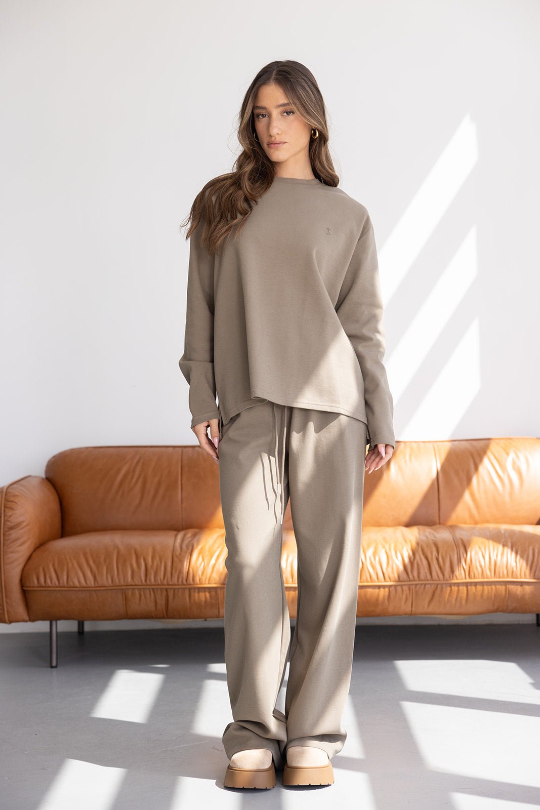 אישה לובשת סט טרנינג בז', חולצה ארוכה ומכנסיים רחבים, אופנת נשים בצילום סטודיו מודרני