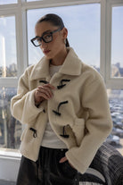 אישה עם משקפיים עבות לובשת מעיל פרווה אופנתי בגוון שמנת בסגנון חורפי, אופנה לנשים