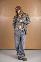 אישה חובשת כובע חום, חולצת פלאנל משובצת, ג'ינס רחב ונעלי חום טרנדיות, אופנת רחוב לנשים