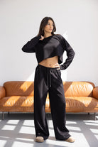 אישה לובשת סט טרנינג שחור אופנתי עם סווטשירט קצוץ ומכנסיים רחבים, עומדת בסלון מואר