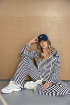 אישה לובשת סט פסים כחול-לבן, כובע כחול ונעלי סניקרס אופנתיות, יושבת ברצפה באווירת אופנה נינוחה