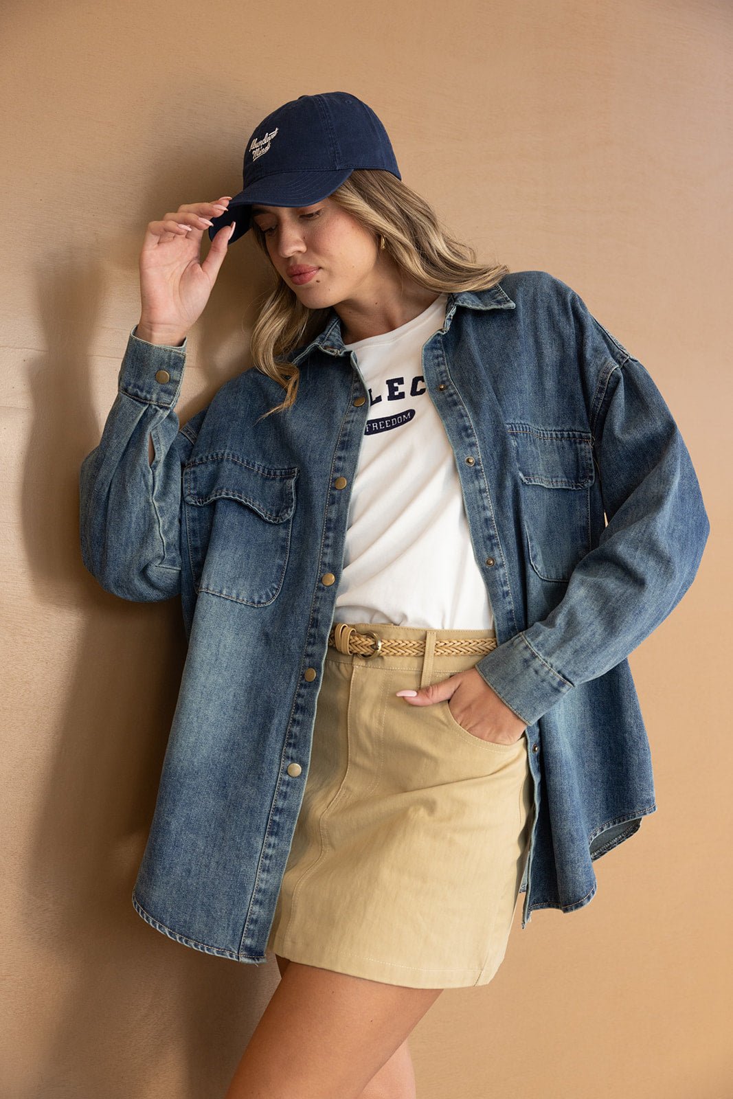 אישה צעירה עם כובע כחול, חולצת טי, חולצה ג'ינס עליונה וחצאית בז', לוק קז'ואל אופנתי לנשים