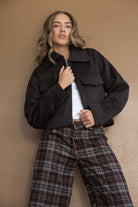 דוגמנית עם ז'קט חום קצר ומכנסי קארו אופנתיים בצבעי חום, רקע נייטרלי, טרנדים חורפיים לנשים