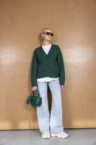 אישה עם קרדיגן ירוק, ג'ינס רחב, תיק ירוק, משקפי שמש ונעלי סניקרס אופנתיות