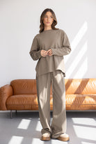 דוגמנית לובשת חליפת טרנינג אופנתית בצבע בז' לנשים, רקע סלון מודרני בהיר