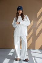 דוגמנית לובשת חליפת טרנינג אפורה לנשים עם כובע כחול ונעלי בית חומות, לוק אופנתי יומיומי