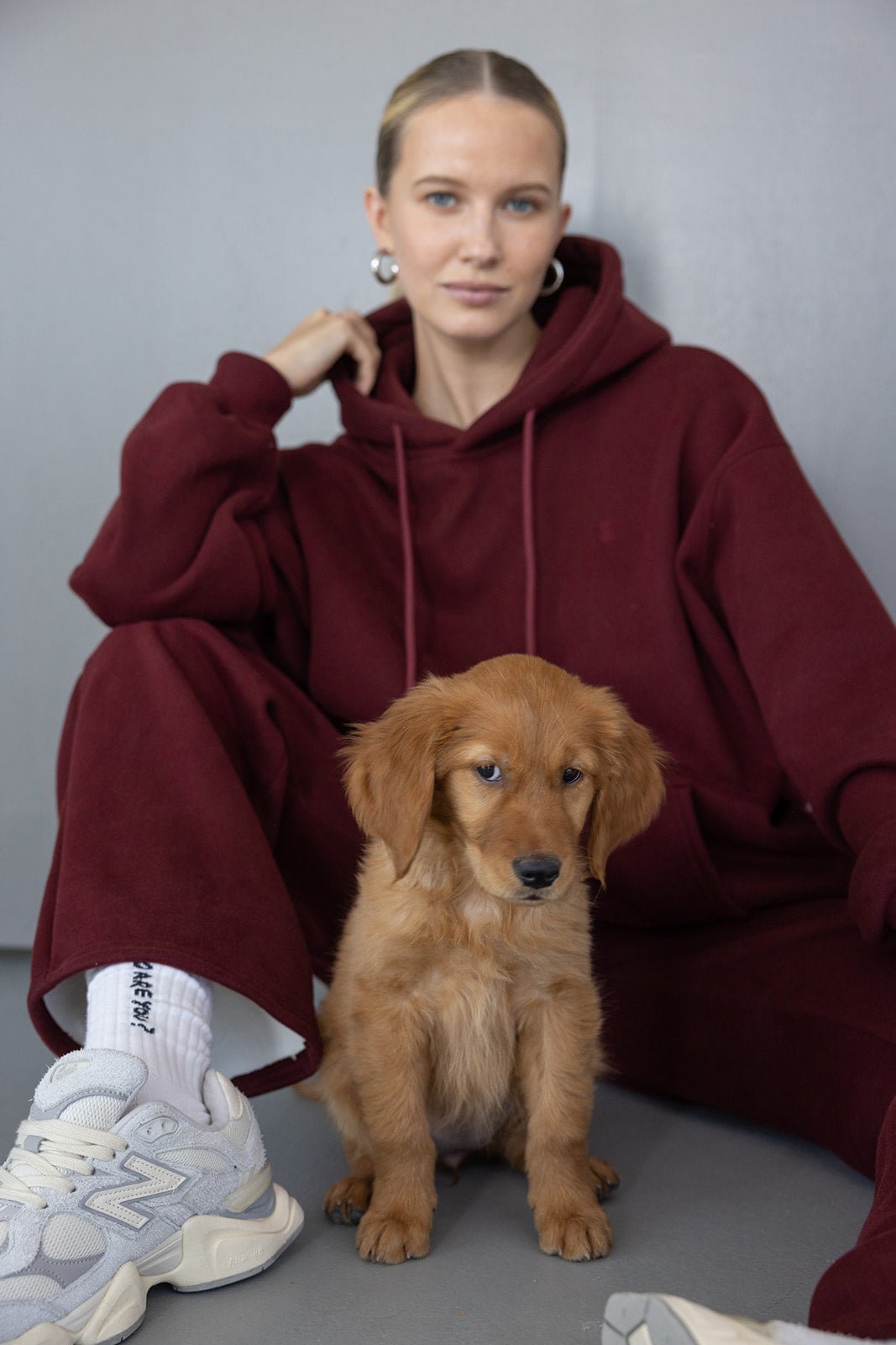 אישה עם קפוצ’ון בורדו אופנתי יושבת לצד כלבלב חום, לוק יום יומי נוח לנשים