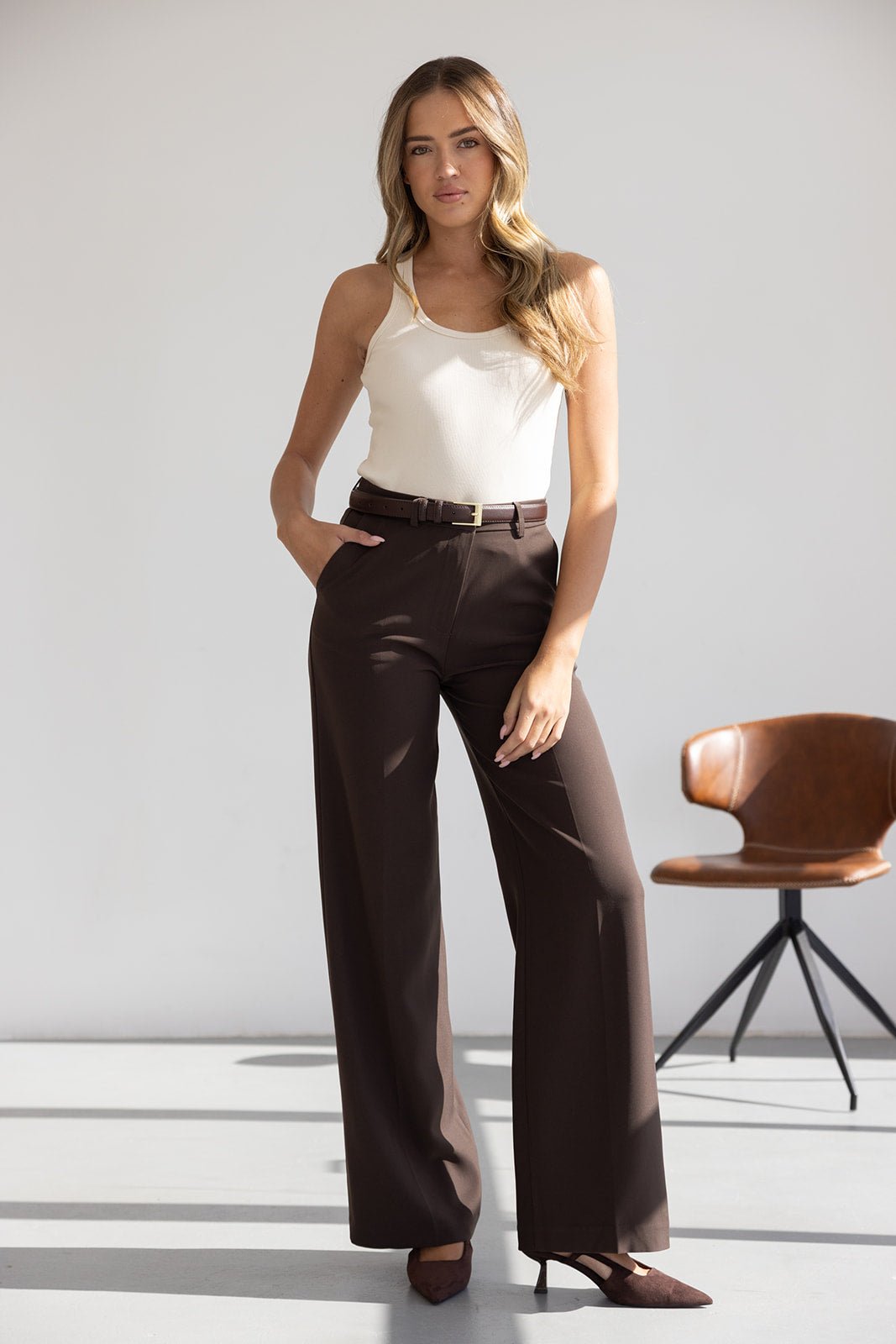 אישה לובשת גופייה לבנה ומכנסיים חומים מחויטים, אופנת נשים מודרנית ליום יום