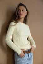 דוגמנית לובשת סוודר צהוב בהיר עם דוגמת צמה, ג'ינס כחול וחגורת חום, אופנת נשים צעירה