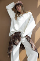 דוגמנית לובשת סט טרנינג בצבע לבן עם חולצה משובצת חומה קשורה למותן וכובע קז'ואל, אופנה לנשים