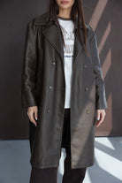 אישה עם מעיל טרנץ' ארוך דמוי עור בצבע חום כהה, חולצה לבנה עם הדפס, סטייל חורפי אופנתי