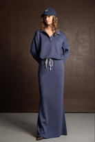 אישה עם שמלה כחולה ארוכה, שרוולים ארוכים, כובע מצחייה כחול, מראה אופנה צעיר ועדכני