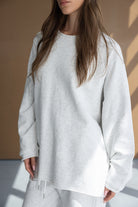 אישה לובשת סט טרנינג אפור בהיר, חולצה ארוכה עם שרוולים ארוכים ומכנסי טרנינג, אופנת נשים נוחה ויומיומית