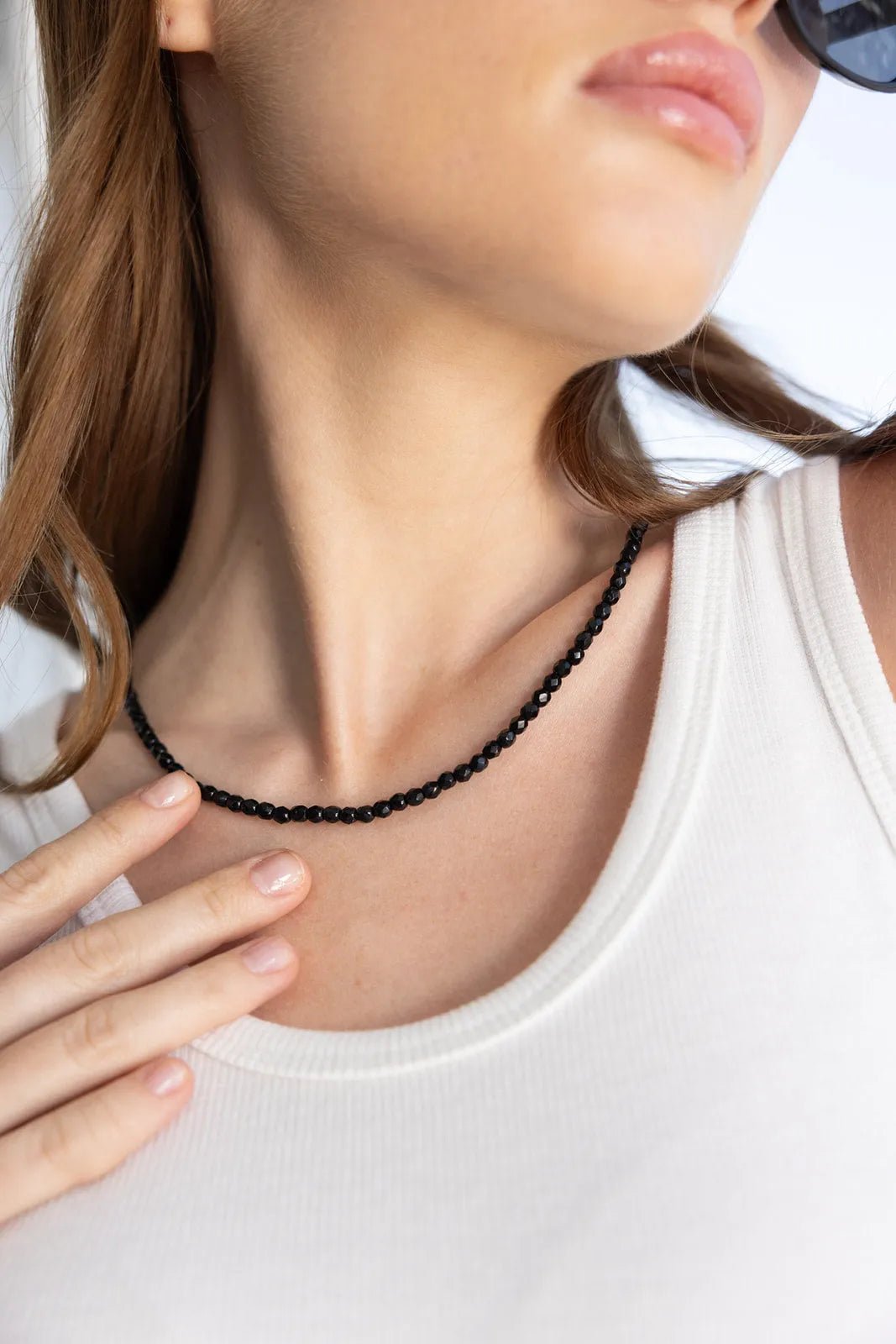 שרשרת חרוזים שחורה אופנתית על צוואר אישה עם גופיה לבנה, אביזרי אופנה לנשים