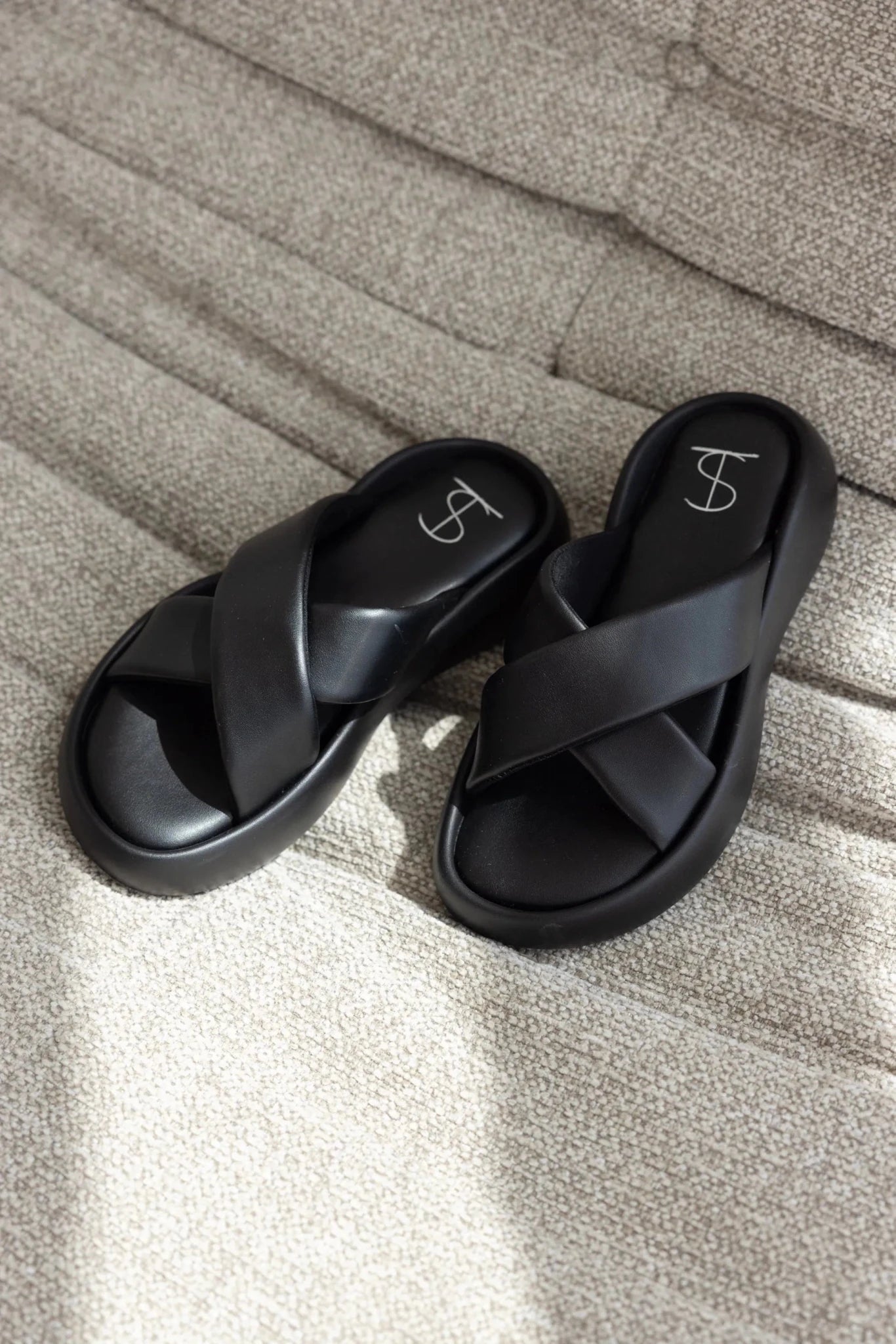 כפכפים שחורים לנשים עם רצועות מוצלבות, מונחים על ספה בהירה, אופנת קיץ לנערות