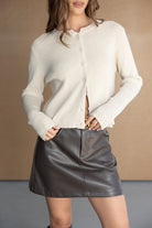 דוגמנית לובשת סוודר נשים בז' עם כפתורים וחצאית מיני דמוי עור שחורה אופנתית