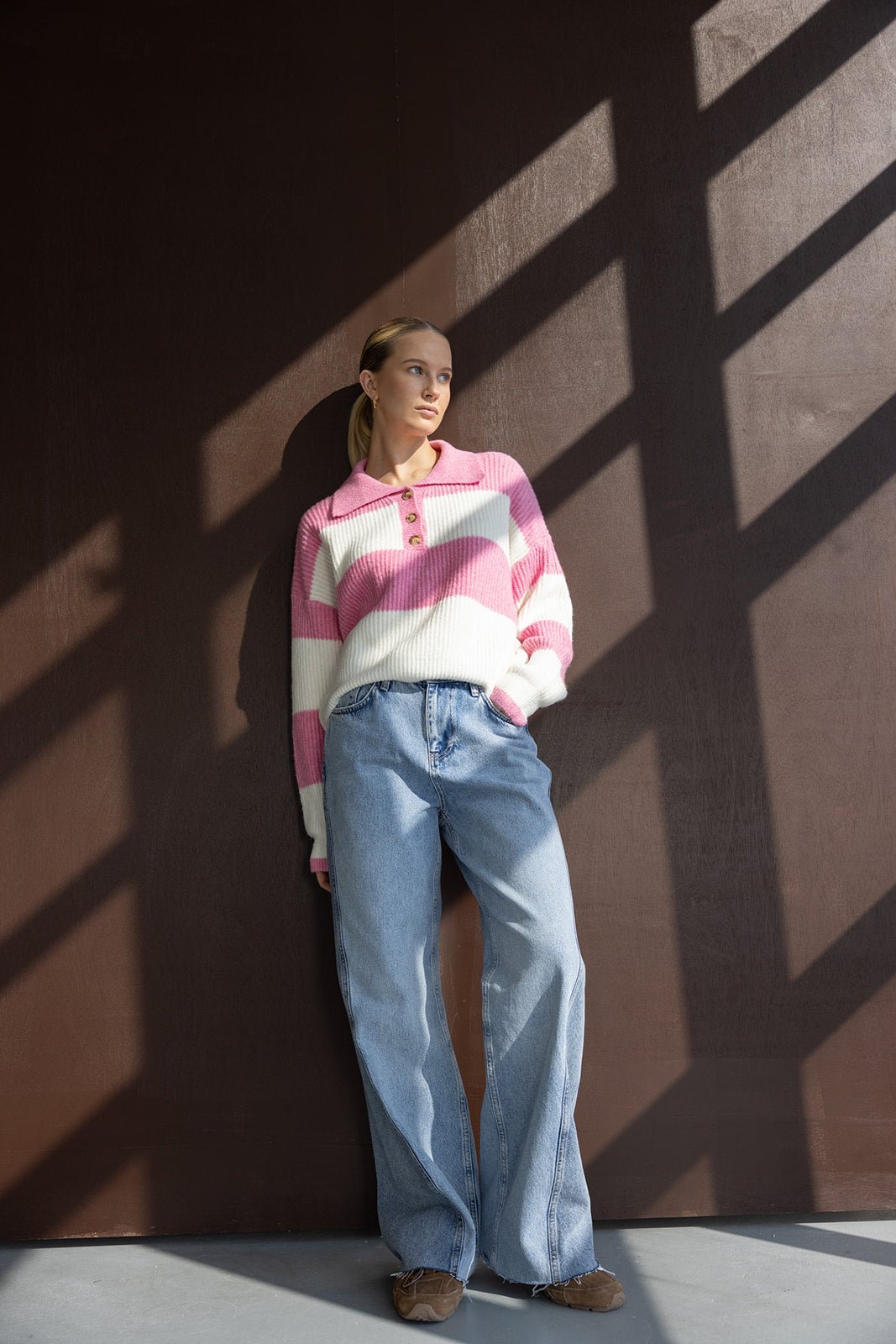 אישה לובשת סוודר פסים ורוד ולבן עם כפתורים ומכנסי ג'ינס רחבים באופנת רחוב צעירה
