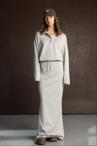 אישה דוגמנית לובשת שמלת סווטשירט אפורה ארוכה עם שרוך, כובע חום ונעלי פלטפורמה חומות, רקע חום