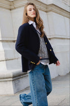 אישה צעירה לובשת ז'קט כחול כהה עם כפתורים זהב, סוודר אפור ומכנסי ג'ינס רחבים, אופנת רחוב לנשים