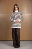 דוגמנית לובשת סוודר פסים אפור חום מעל חולצה לבנה ומכנסיים רחבים חומים, אופנת חורף לנשים