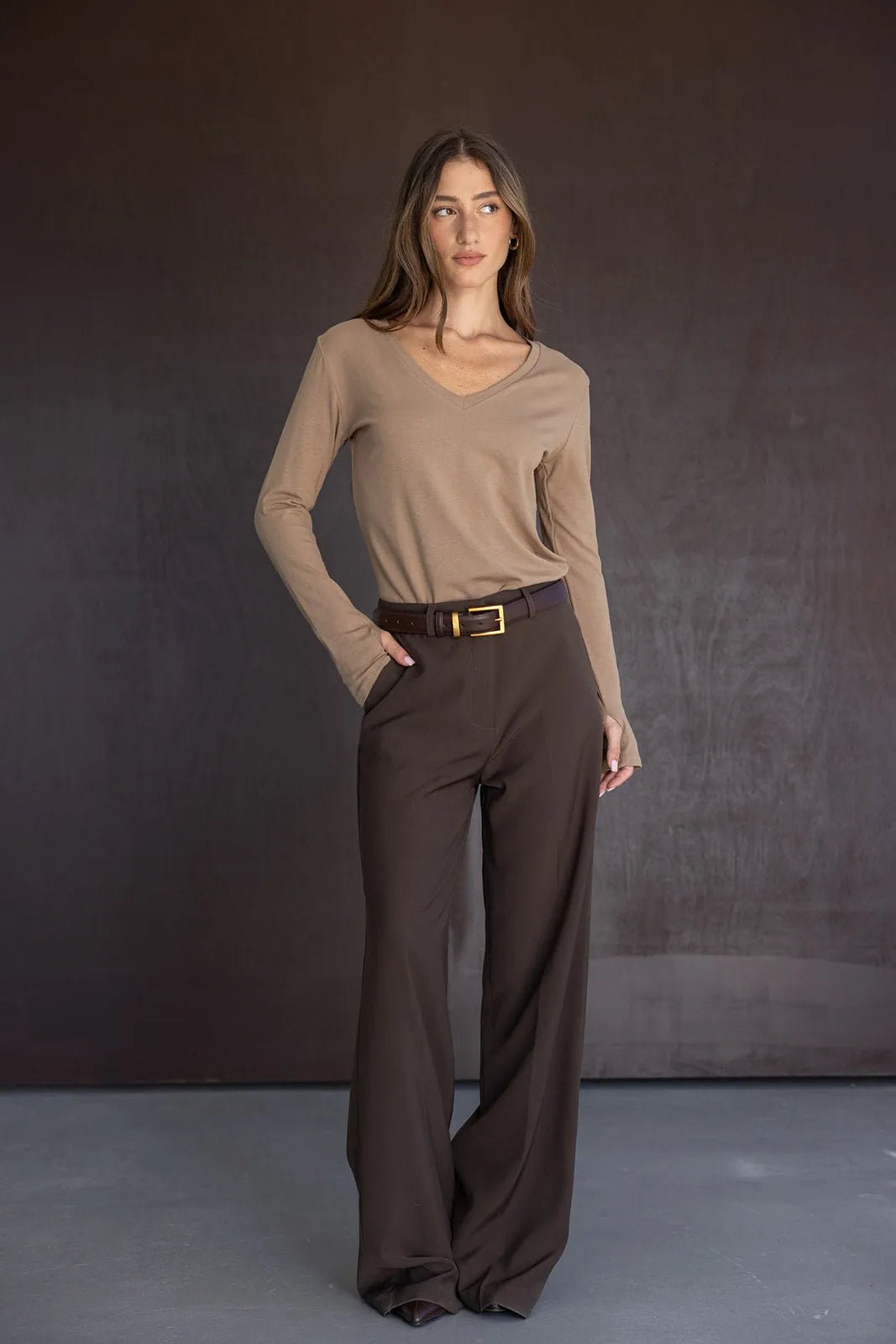 דוגמנית לובשת חולצה בצבע בז' עם שרוולים ארוכים, מכנסיים מחויטים חומים וחגורה אופנתית