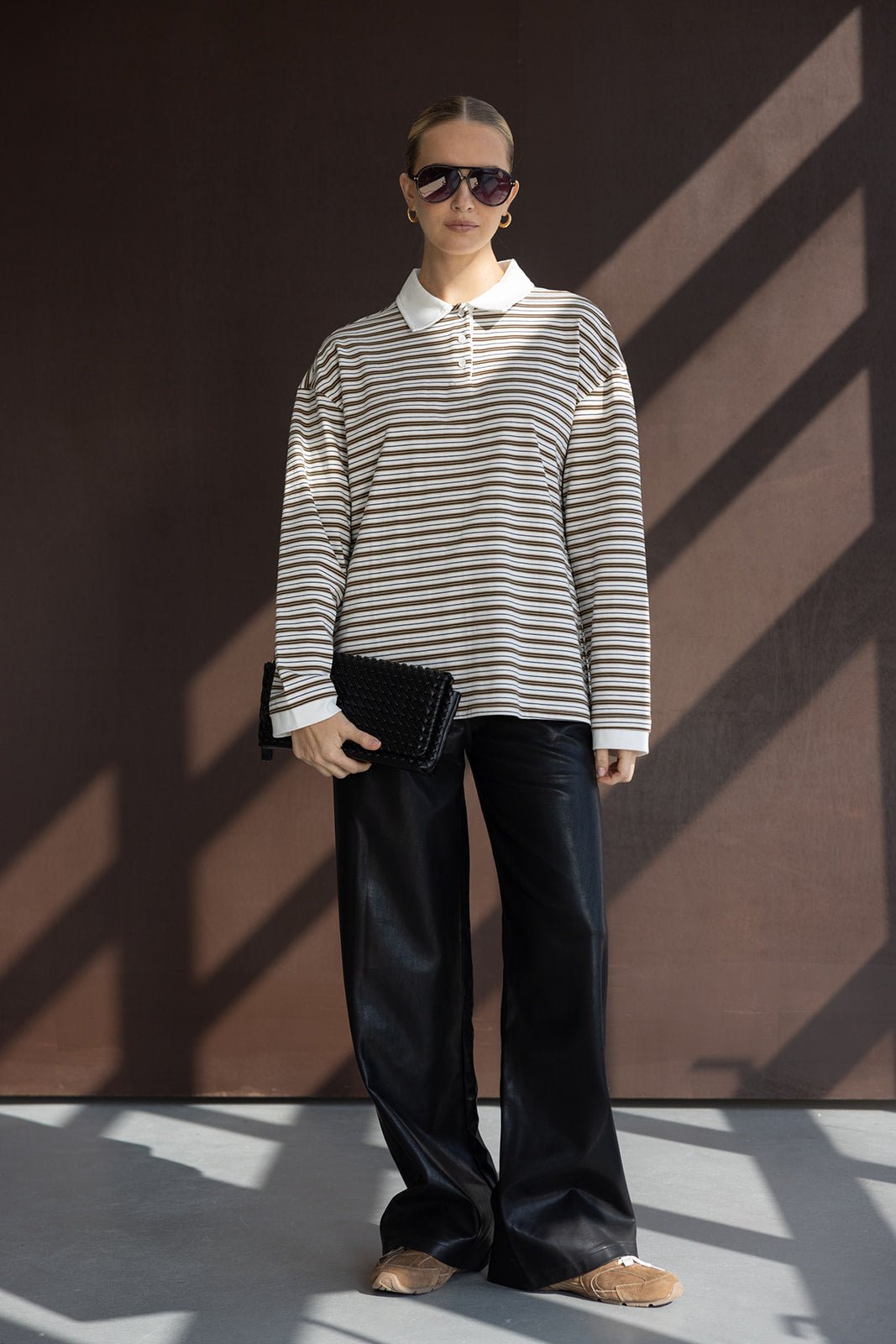 אישה עם חולצה פסים ארוכה, מכנסיים שחורים רחבים, תיק קלאץ' ומשקפי שמש אופנתיים