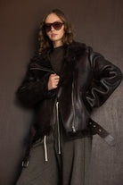 דוגמנית לובשת מעיל עור חום אופנתי עם רוכסן, משקפי שמש וחולצה כהה, אופנת חורף לנשים