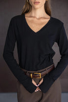 חולצת נשים שחורה עם שרוולים ארוכים ומחשוף וי, מכנסיים חומים וחגורת עור חום