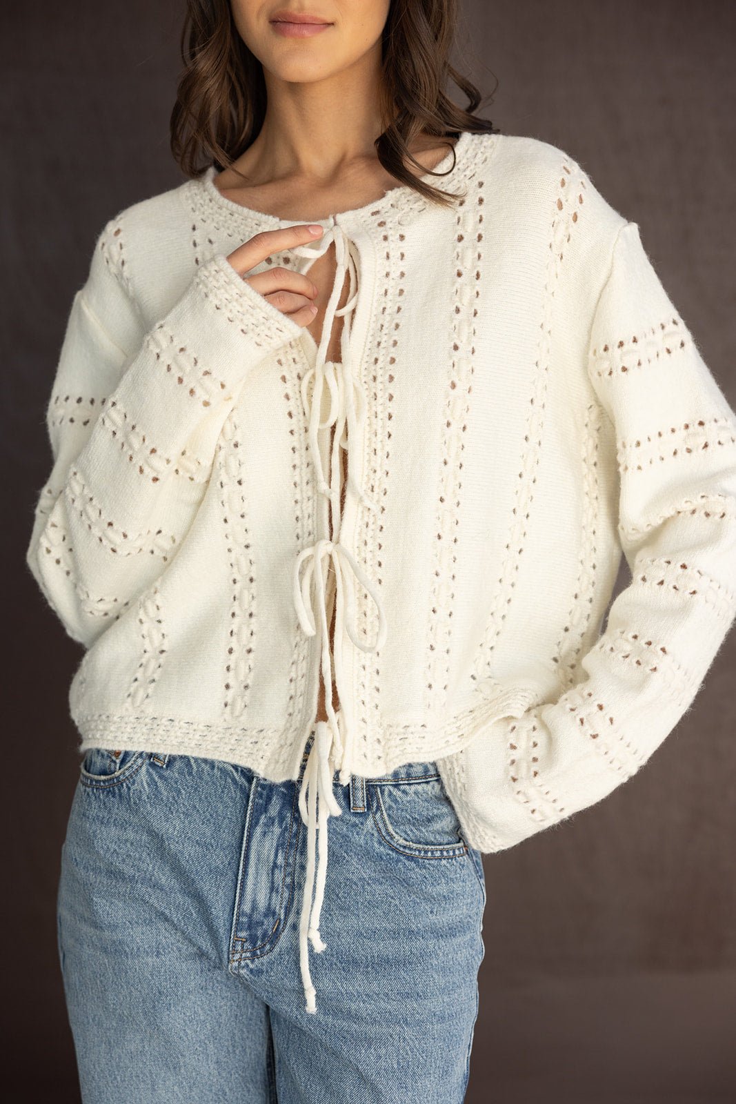 סוודר לבן סרוג עם שרוכים לקשירה, ג'ינס בגזרת מותן גבוהה, אופנה נשית עכשווית