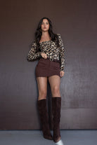 אישה לובשת בגד גוף מנומר עם חצאית מיני חומה ומגפיים גבוהים חומים, אופנת נשים עדכנית