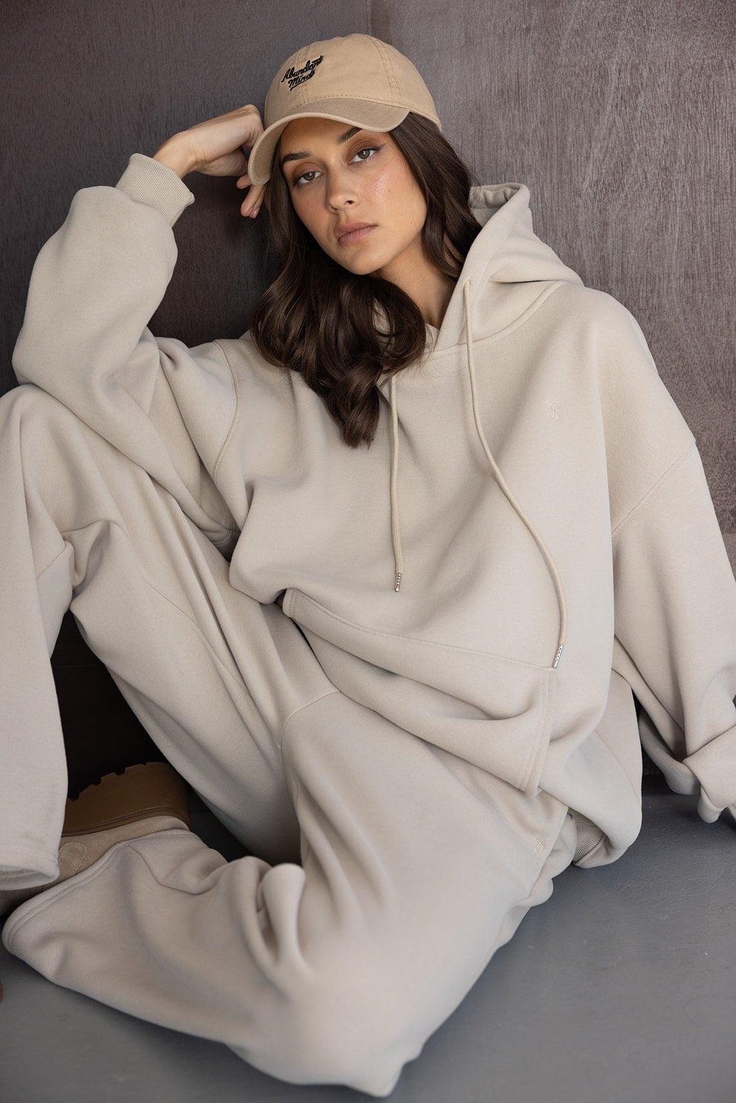 אישה לובשת סט טרנינג בז' עם קפוצ'ון וכובע מצחייה, לוק קז'ואל אופנתי לנשים